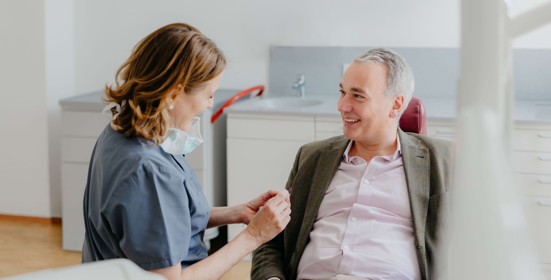 Dr. med. dent Maren Seubert unterh&auml;lt sich mit einem &auml;lteren Patient, der auf dem Behandlungsstuhl in der Karlsruher Praxis sitzt.