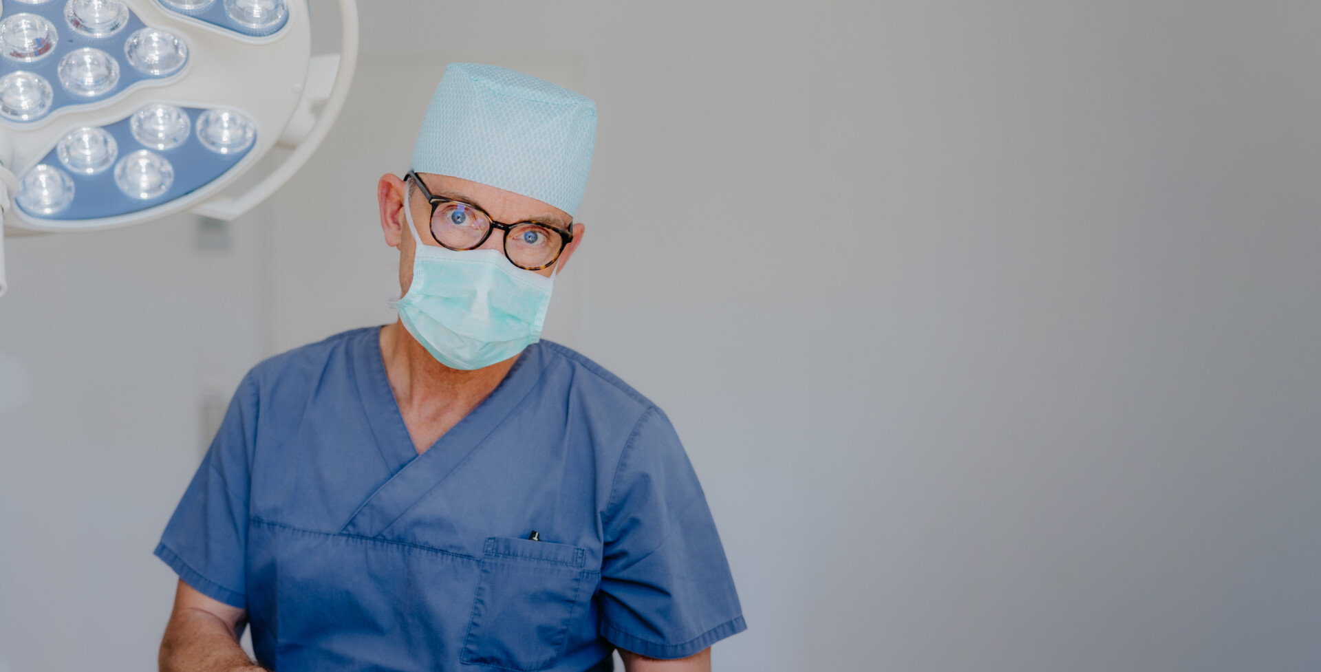 Prof. Schierle sitzt in hellgrauem Kasak und mit OP-Haube und Mundschutz im OP-Saal seiner oralchirurgischen Praxis in der Karlsruher Weststadt