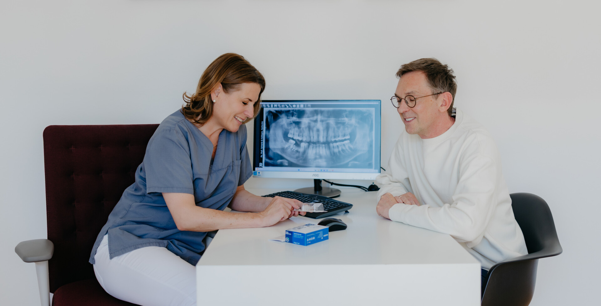 Dr. med. dent. Maren Seubert zeigt einem Patienten ein Keramikimplantat und erl&auml;utert die Einbringung in den Kiefer.