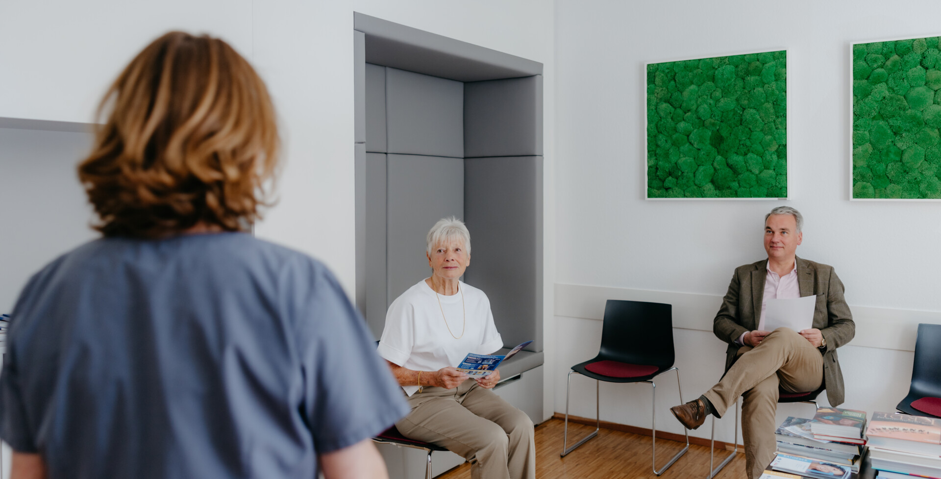 Blick ins freundliche Wartezimmer von C.WEST, in dem zwei Patient:innen sitzen und von der freundlichen &Auml;rztin aufgerufen werden.
