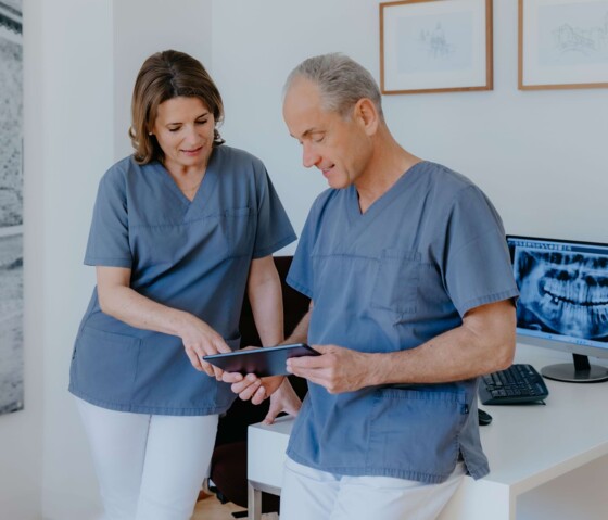 Dr. Maren Seubert und Dr. Hannes Schierle in blauen Kasacks schauen gemeinsam auf ein Tablet.