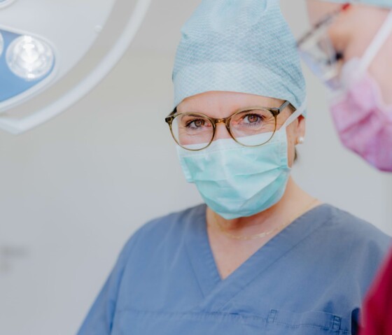 Zahn&auml;rztin in blauer OP-Kleidung bespricht sich am Operationstisch &uuml;ber einer Ablage mit sterilen Instrumenten.